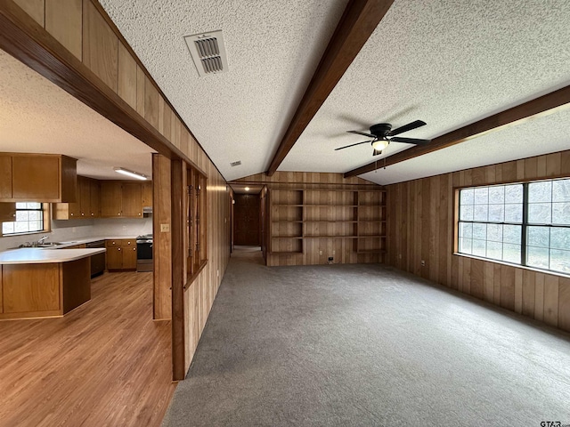 unfurnished living room featuring vaulted ceiling with beams, sink, a textured ceiling, and wood walls