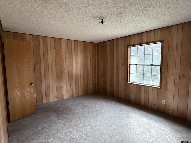 carpeted empty room featuring a textured ceiling and wood walls