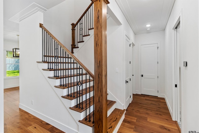 stairs featuring hardwood / wood-style floors, crown molding, and an inviting chandelier