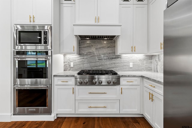 kitchen featuring light stone countertops, premium range hood, stainless steel appliances, dark hardwood / wood-style floors, and white cabinetry