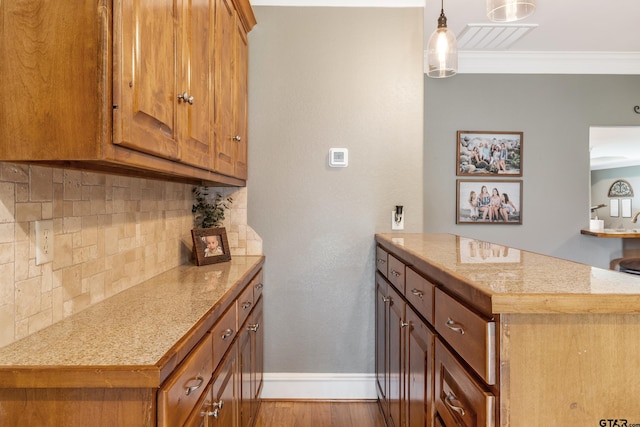 kitchen with kitchen peninsula, ornamental molding, backsplash, decorative light fixtures, and light hardwood / wood-style flooring