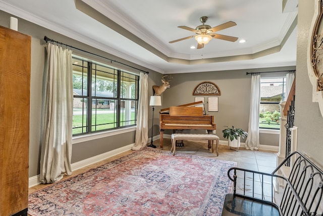 living area with light tile patterned flooring, ceiling fan, a raised ceiling, and crown molding