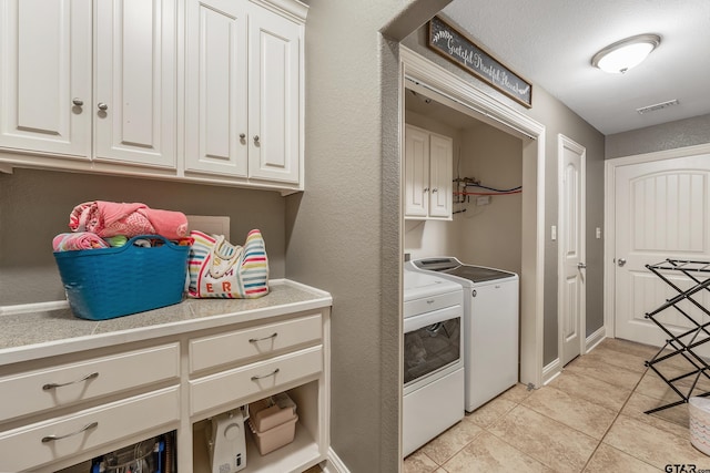 clothes washing area with washing machine and dryer, cabinets, and light tile patterned floors