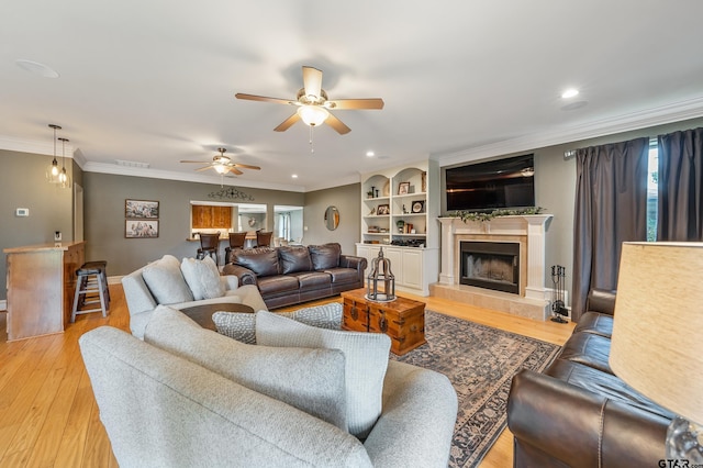 living room with a fireplace, light hardwood / wood-style floors, ceiling fan, and crown molding