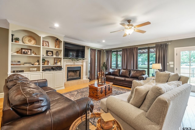 living room featuring ceiling fan, a tile fireplace, light wood-type flooring, and ornamental molding