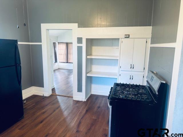 kitchen with dark wood-type flooring, black refrigerator, white cabinetry, and stainless steel gas range