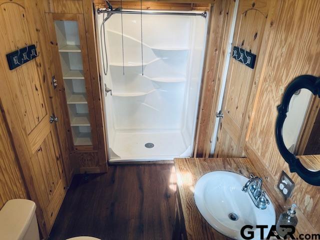 bathroom featuring toilet, wood walls, sink, and walk in shower