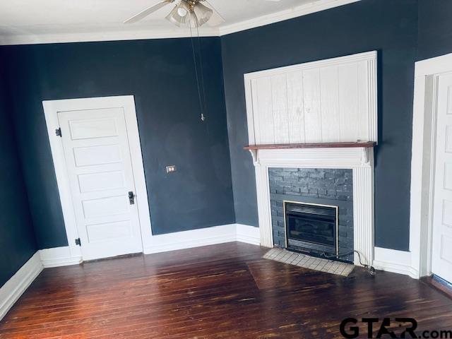 unfurnished living room featuring ceiling fan, ornamental molding, dark hardwood / wood-style floors, and a stone fireplace