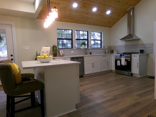 kitchen with pendant lighting, a kitchen breakfast bar, wall chimney exhaust hood, kitchen peninsula, and stainless steel appliances