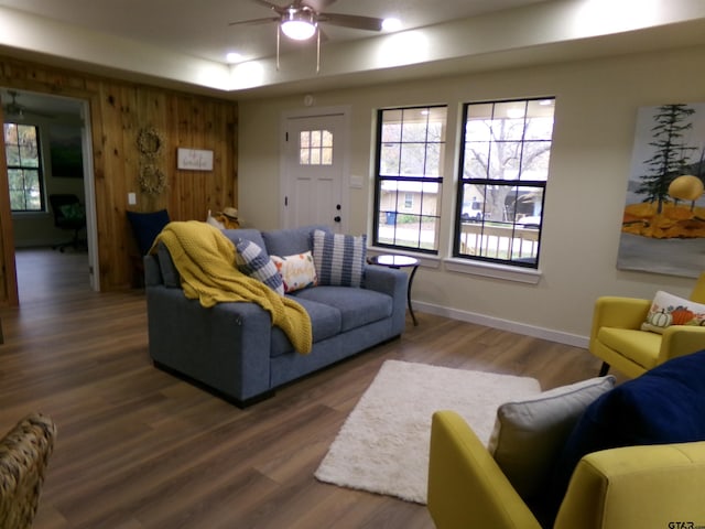 living room featuring ceiling fan, wooden walls, and dark wood-type flooring