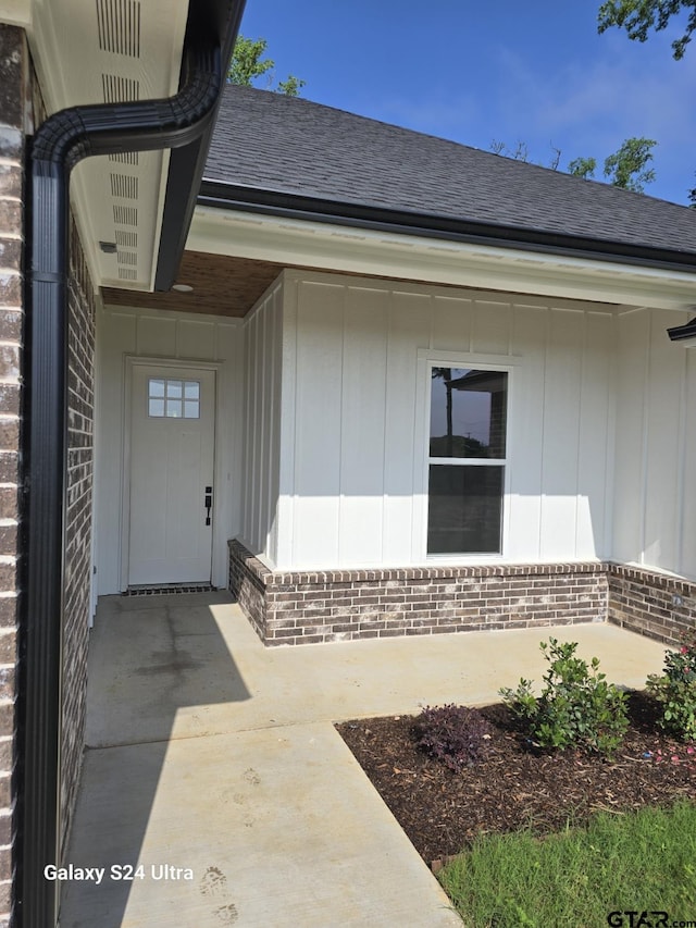 property entrance featuring brick siding and roof with shingles