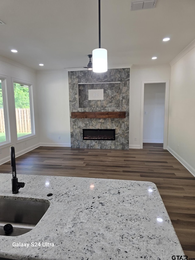 unfurnished living room with crown molding, a fireplace, wood finished floors, a sink, and baseboards