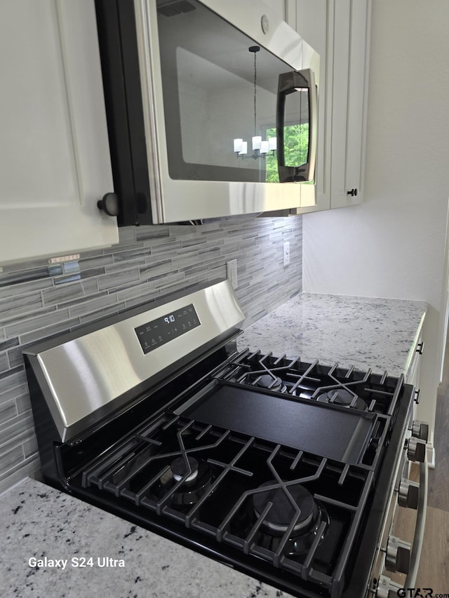room details featuring white cabinets, stainless steel appliances, light stone countertops, and backsplash
