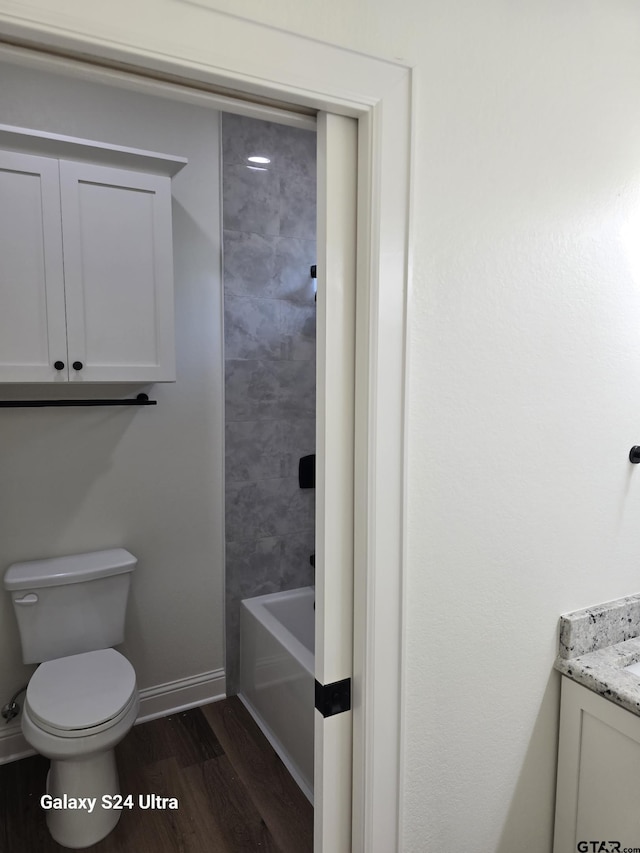 bathroom featuring vanity, wood finished floors, toilet, baseboards, and a tub
