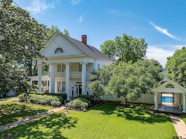 neoclassical home featuring a front lawn, ceiling fan, and a balcony