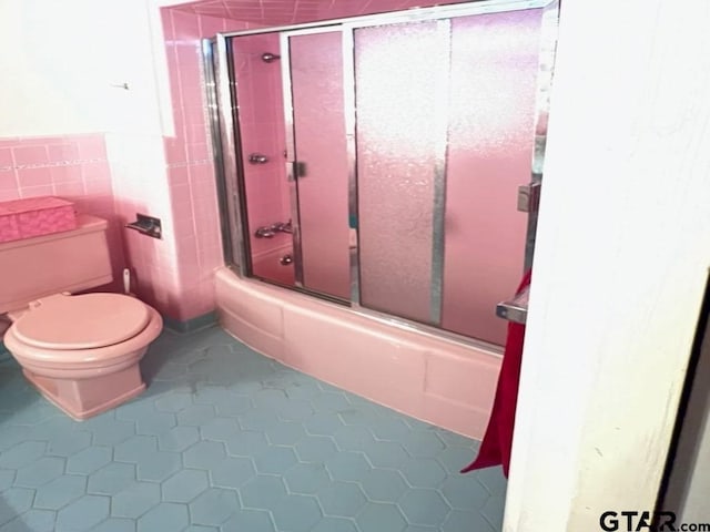 bathroom with toilet, tile patterned floors, and bath / shower combo with glass door