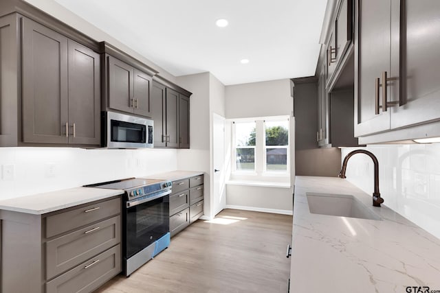 kitchen with light stone countertops, sink, tasteful backsplash, light hardwood / wood-style floors, and appliances with stainless steel finishes