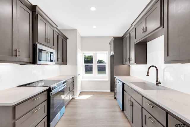 kitchen with sink, light stone counters, backsplash, light hardwood / wood-style floors, and appliances with stainless steel finishes