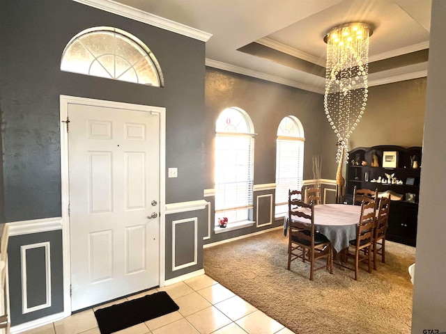 entrance foyer with a tray ceiling, light tile patterned floors, ornamental molding, and a notable chandelier