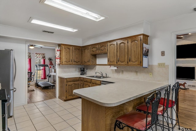 kitchen featuring sink, stainless steel appliances, light tile patterned flooring, decorative backsplash, and kitchen peninsula