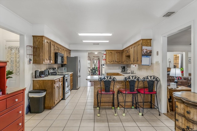 kitchen with a kitchen bar, sink, light tile patterned floors, kitchen peninsula, and stainless steel appliances