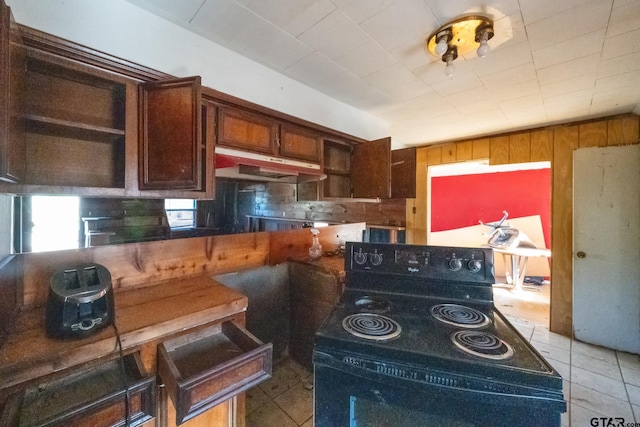 kitchen with electric range, wood walls, under cabinet range hood, and light tile patterned flooring