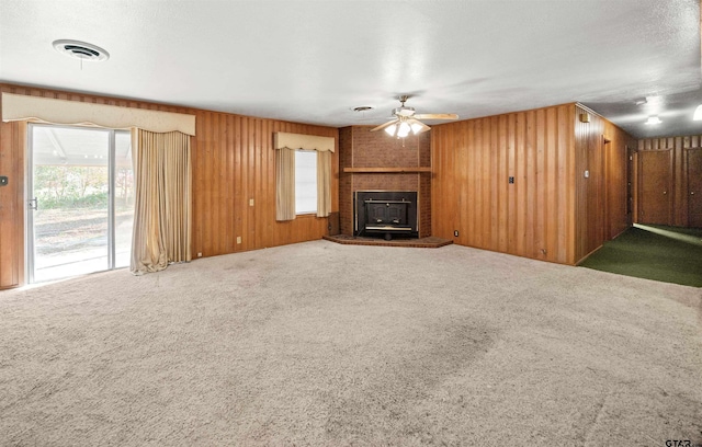 unfurnished living room featuring ceiling fan, wooden walls, carpet floors, and a brick fireplace