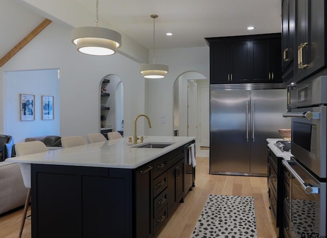 kitchen with arched walkways, pendant lighting, appliances with stainless steel finishes, a kitchen island with sink, and a sink