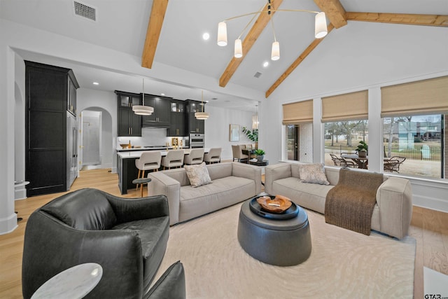 living room with arched walkways, light wood finished floors, visible vents, high vaulted ceiling, and beamed ceiling