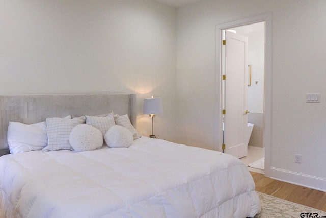 bedroom with ensuite bath, light wood-style flooring, and baseboards