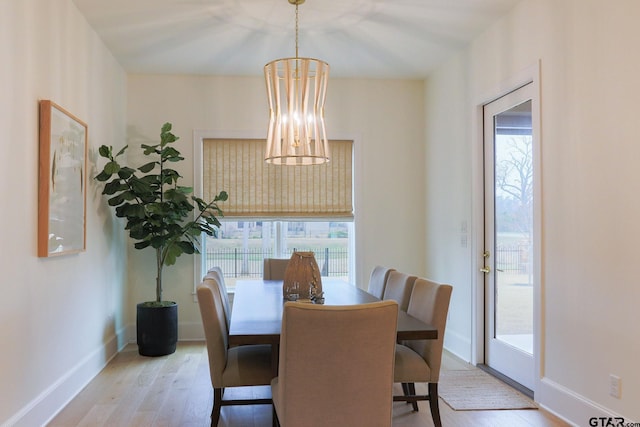 dining space with light wood-type flooring, a notable chandelier, and baseboards