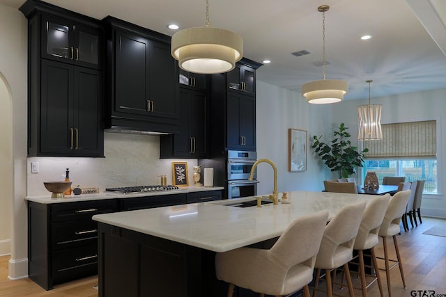 kitchen featuring a kitchen island with sink, dark cabinets, visible vents, appliances with stainless steel finishes, and decorative light fixtures