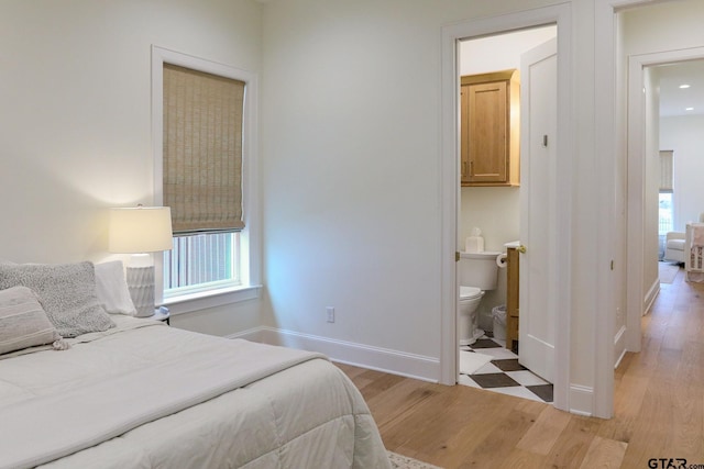 bedroom featuring baseboards, light wood finished floors, and ensuite bathroom