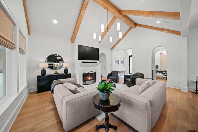 living room with arched walkways, high vaulted ceiling, a ceiling fan, light wood-style floors, and a lit fireplace