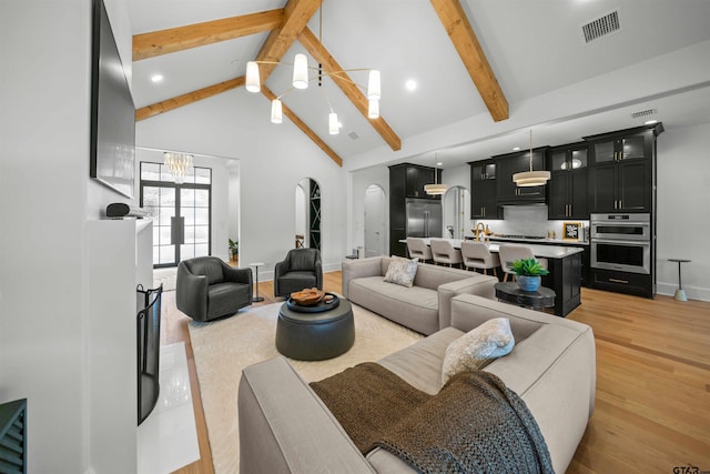 living area featuring arched walkways, visible vents, light wood-style flooring, a chandelier, and beamed ceiling