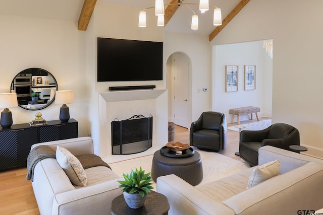 living area featuring vaulted ceiling with beams, a fireplace with flush hearth, arched walkways, and wood finished floors