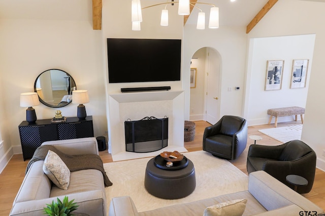 living room with arched walkways, a fireplace, baseboards, light wood finished floors, and beamed ceiling