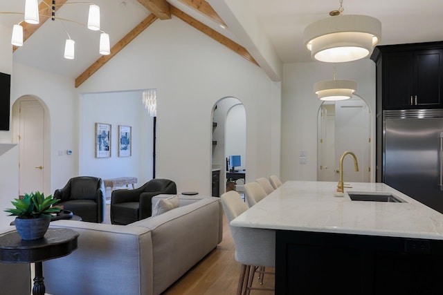 kitchen featuring dark cabinets, arched walkways, a sink, and a center island with sink