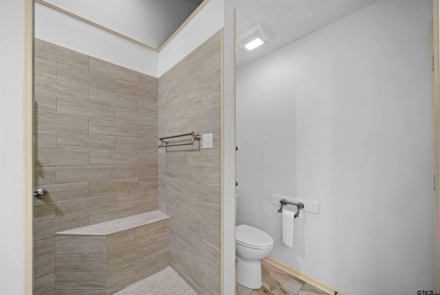 bathroom featuring tiled shower, toilet, and tile patterned floors