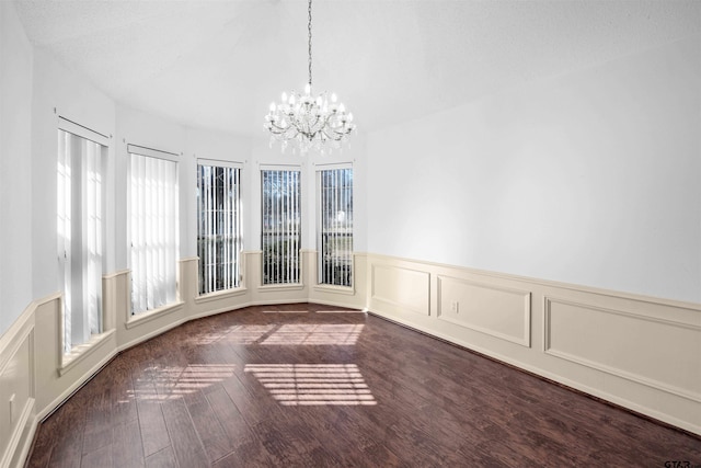 unfurnished dining area featuring a chandelier, plenty of natural light, wood finished floors, and a decorative wall