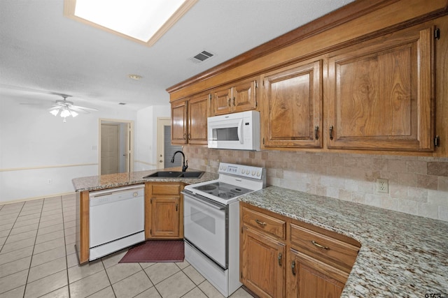 kitchen featuring light tile patterned floors, a peninsula, white appliances, and a sink