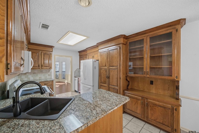 kitchen featuring light tile patterned floors, white appliances, a sink, visible vents, and brown cabinets