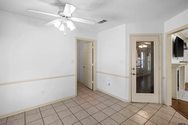 unfurnished room featuring a textured ceiling, ceiling fan, light tile patterned flooring, visible vents, and baseboards