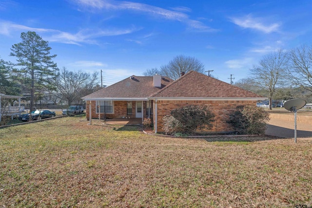 rear view of property with a yard, a shingled roof, and brick siding