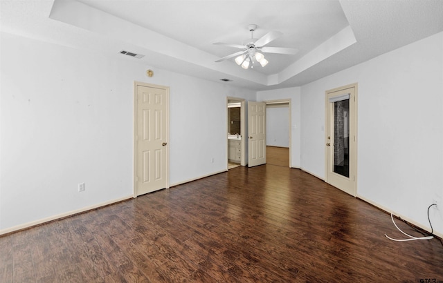 empty room with a raised ceiling, visible vents, ceiling fan, wood finished floors, and baseboards