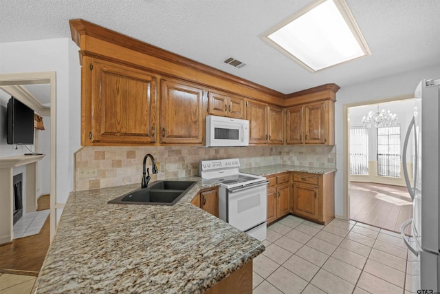 kitchen with light tile patterned floors, visible vents, brown cabinetry, a sink, and white appliances