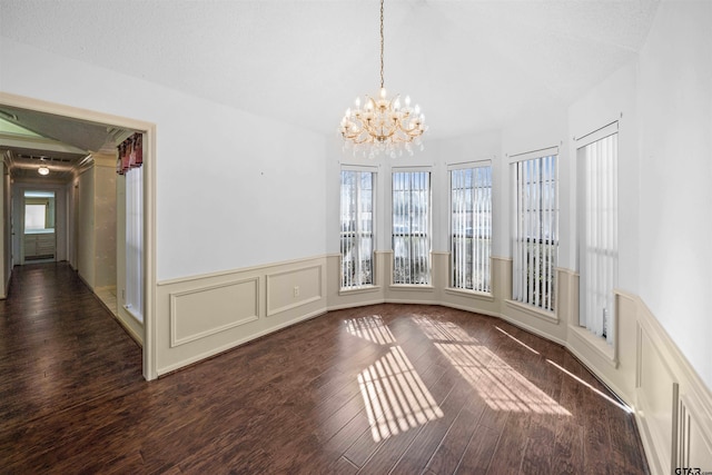 unfurnished dining area featuring a wainscoted wall, a decorative wall, wood finished floors, and a chandelier