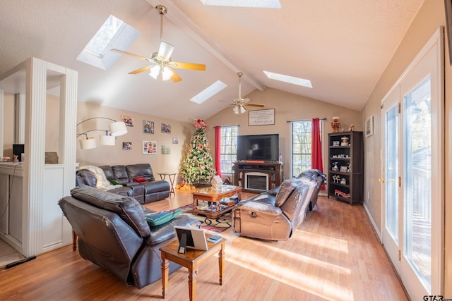 living room with a fireplace, ceiling fan, hardwood / wood-style floors, and vaulted ceiling with skylight