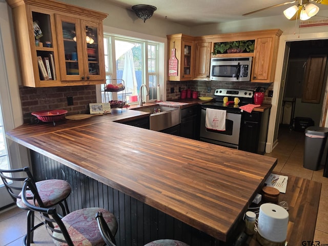 kitchen with appliances with stainless steel finishes, tasteful backsplash, butcher block countertops, light tile patterned flooring, and kitchen peninsula