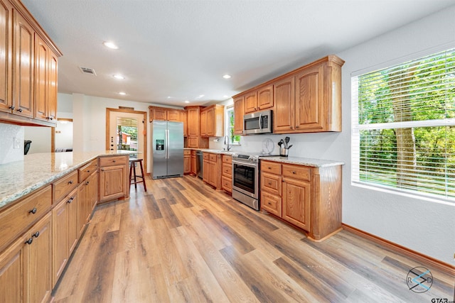 kitchen featuring stainless steel appliances, sink, light hardwood / wood-style floors, and light stone counters